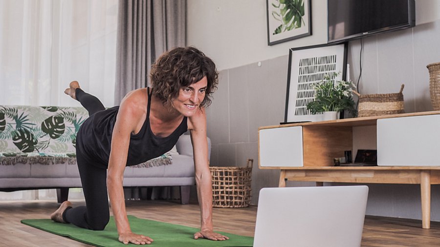 Frau bei Pilates-Übungen vor ihrem Laptop in einem Wohnzimmer