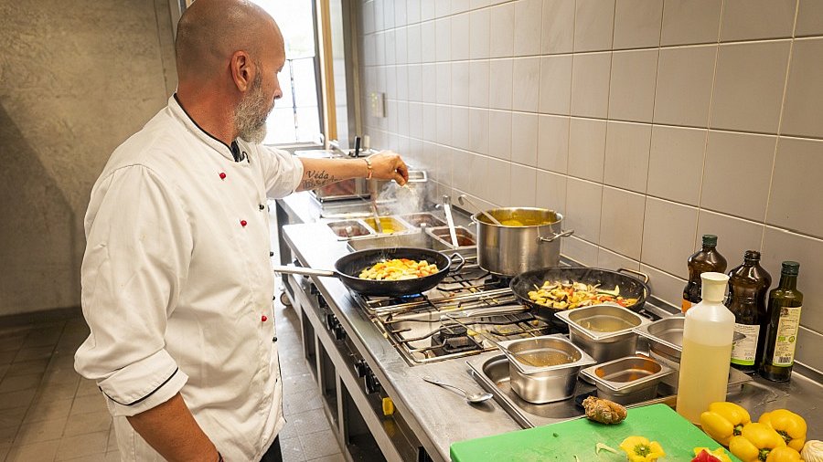 Koch in einer Großküche würzt das Essen in einer Pfanne.