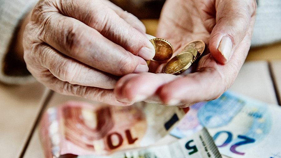 Bildausschnitt von Händen eines älteren Menschen, die Münzgeld halten.