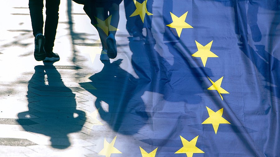 Blaue EU-Fahne mit Sternen, daben Schatten von gehenden Menschen