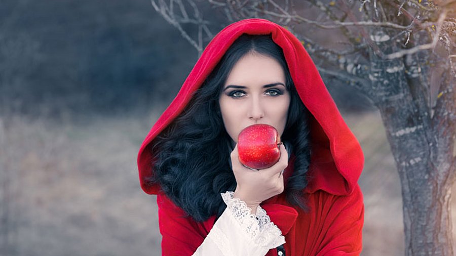 Frau mit roten Mantel, beißt in einen roten Apfel.