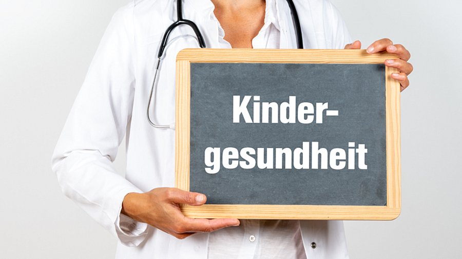 Ärztin (Brustbild) hält Schild mit der Aufschrift "Kindergesundheit" vor sich