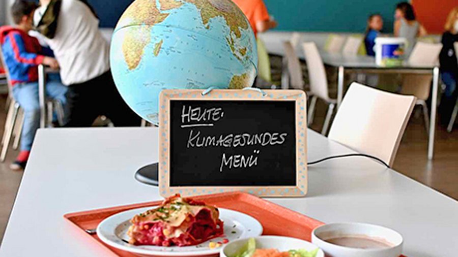 In einem Klassenraum stehen ein Globus, eine Kreidetafel und drei Teller mit Essen.