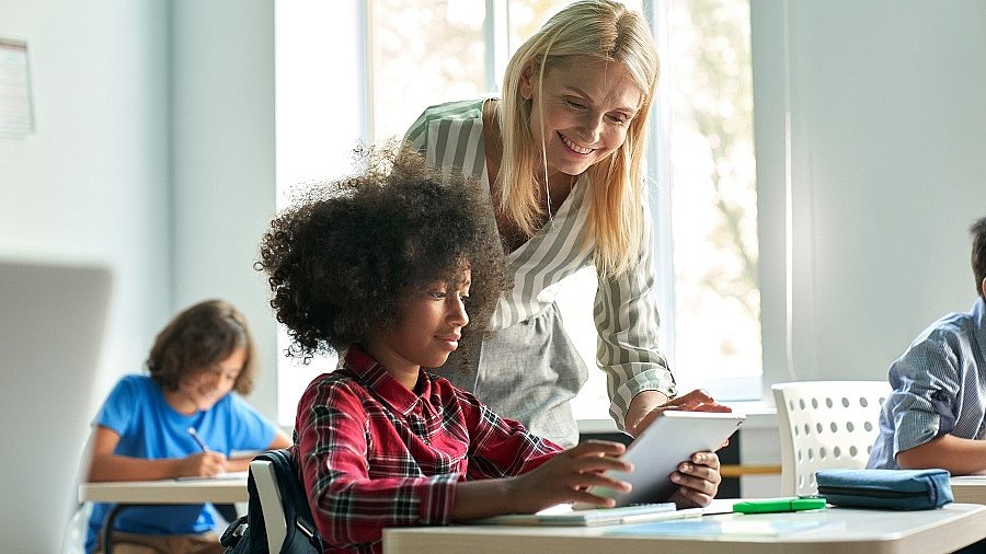Junge Lehrerin zeigt Kind am Platz etwas auf einem Tablet.