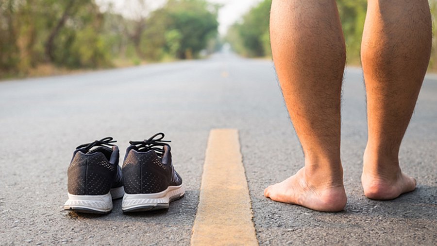 Nackte Füße und Sportschuhe auf einer Asphalt-Straße