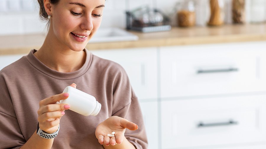 Junge Frau schüttelt sich Kapseln aus einer Packung in die Hand